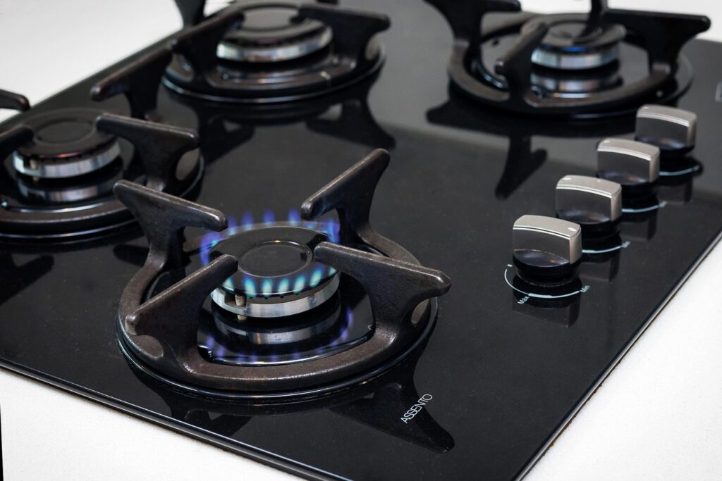 Black glass gas cooktop with one burner lit and a clean blue flame