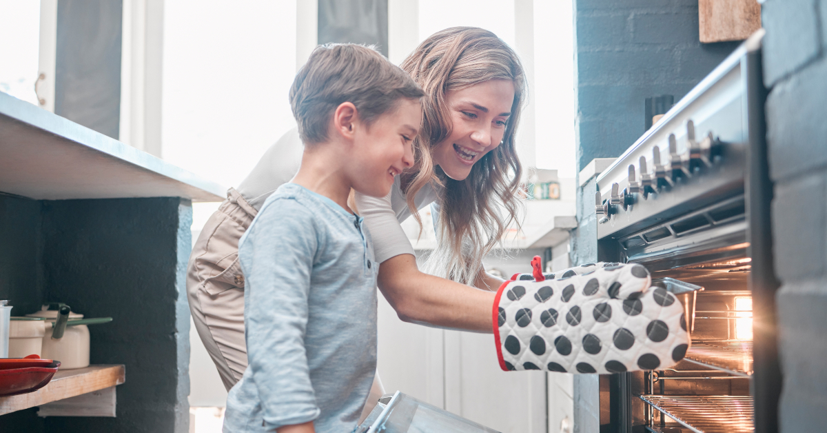 A mother and son taking a tray out of a working oven in a home kitchen