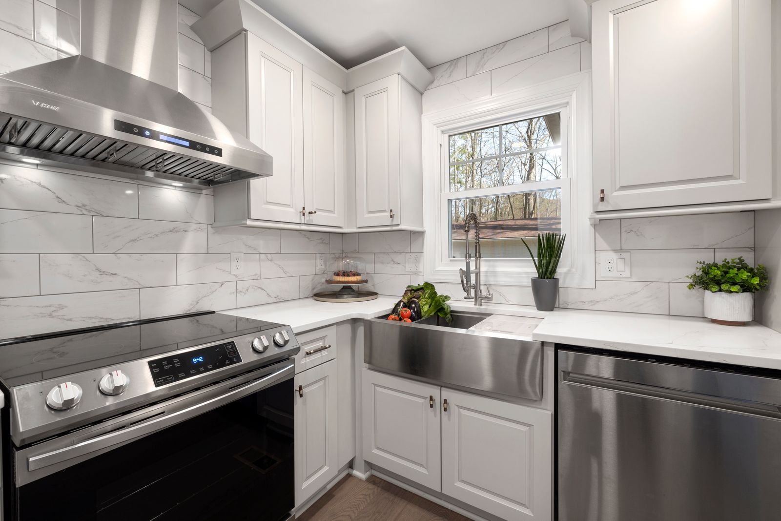 Stainless steel canopy rangehood with baffle filters above a kitchen bench, with white cabinets and marble-look tiles